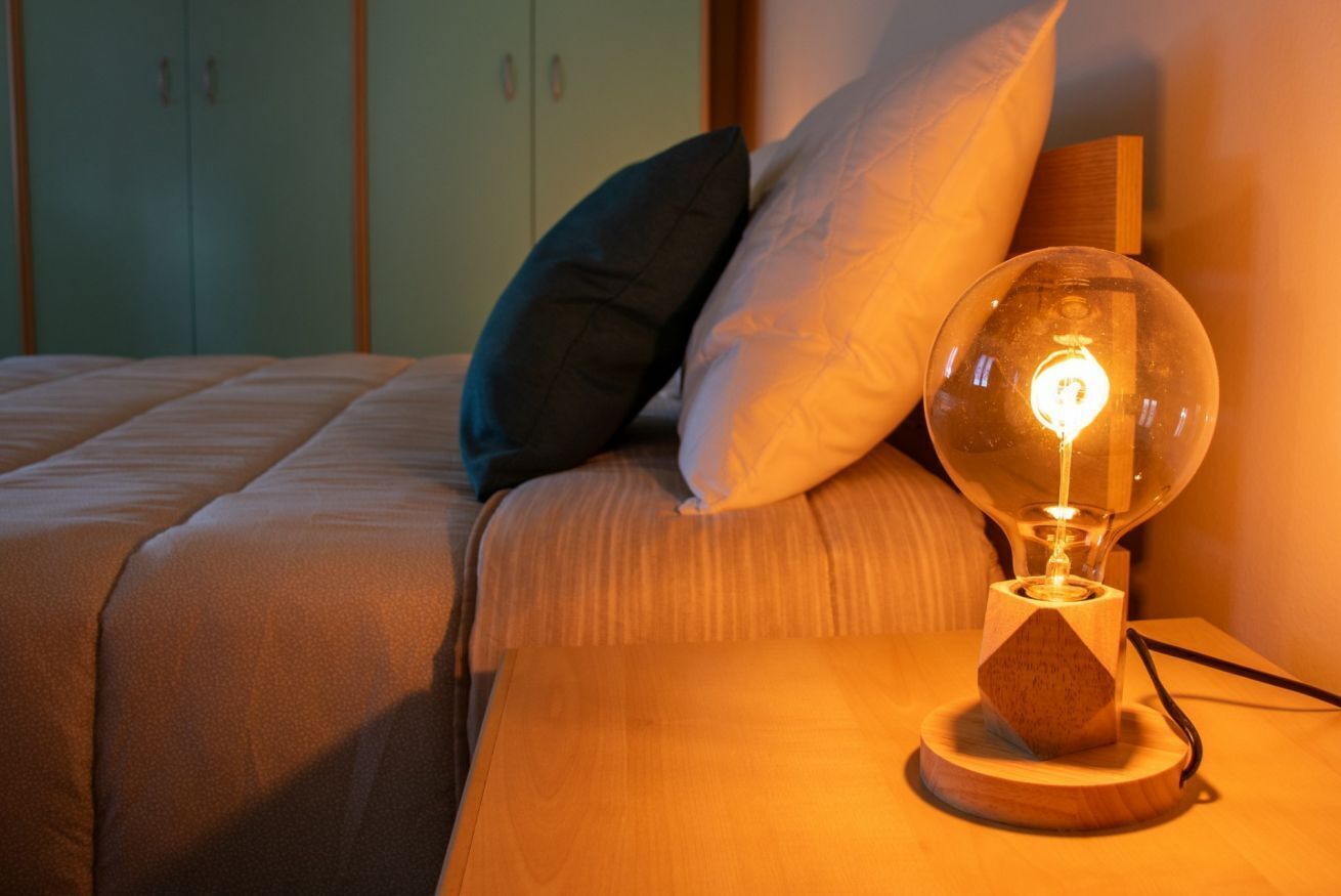 Ein Bett mit Kissen, ein Nachttisch mit Lampe und ein Schrank im Hintergrund.