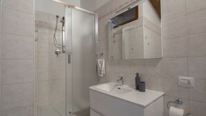 A modern bathroom with a glass shower enclosure, a white vanity with a sink, and a mirror above the vanity.
