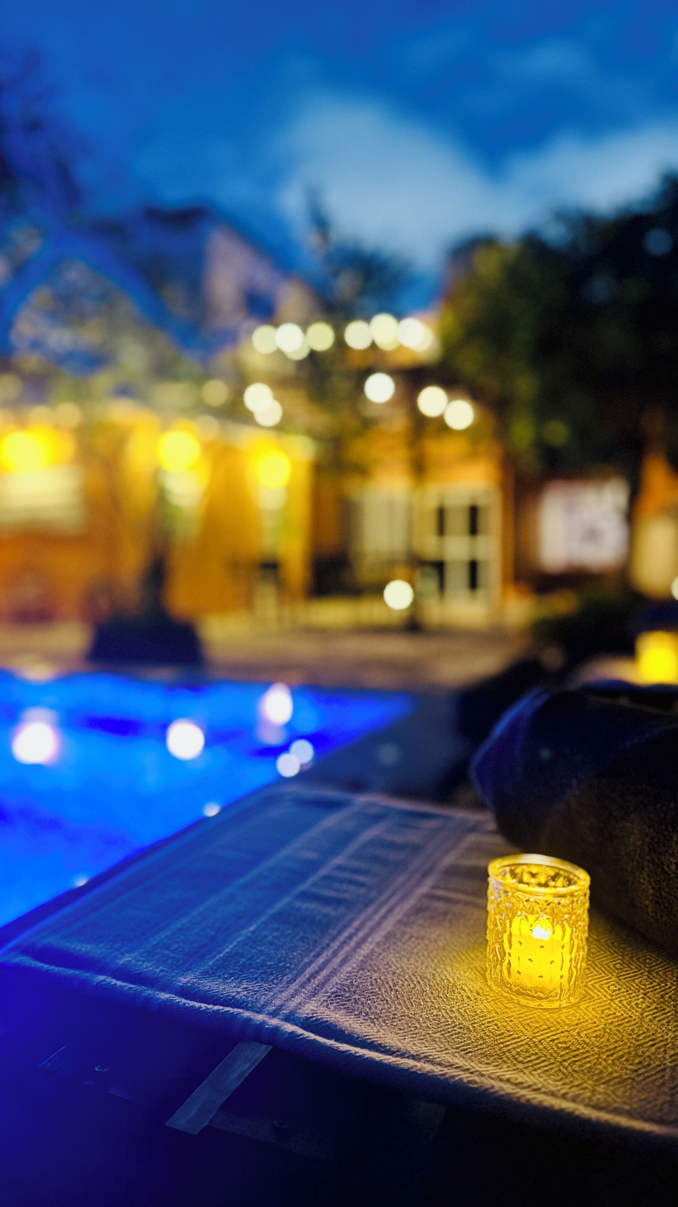 A pool area with a candle on a lounge chair, surrounded by blurred lights and buildings.