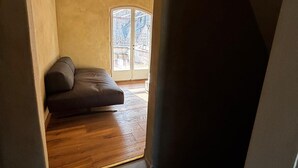 Avoin, loft-tyylinen huone, jossa on puulattia, tumma sohva ja suuri ikkuna.
