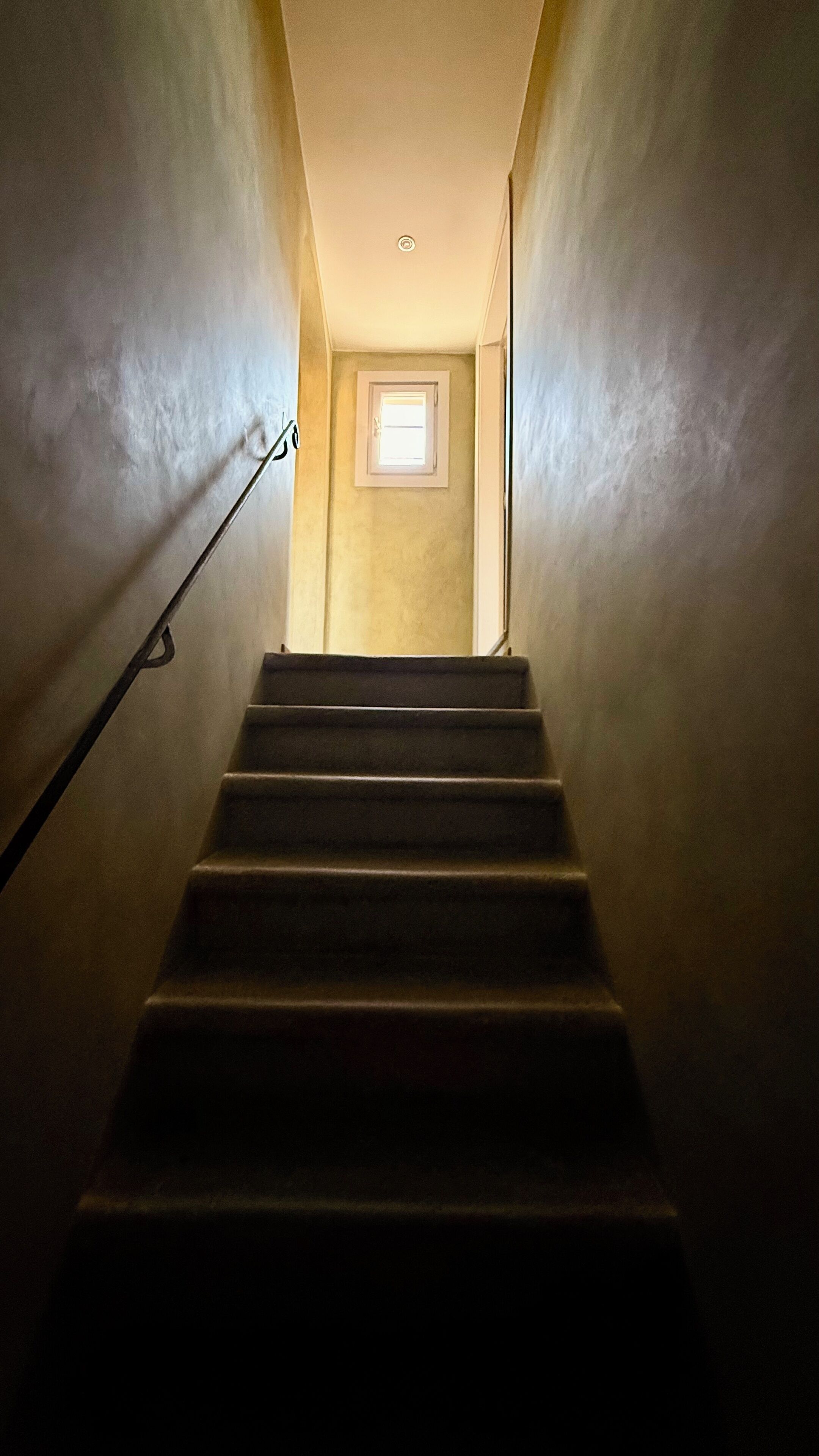 A staircase with a handrail leading to a landing with a small window.