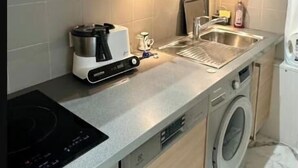 A compact kitchen with a built-in stove, a coffee maker, a sink, and a washing machine. - AN EXCEPTIONAL PARISIAN EXPERIENCE CLOSE TO ODEAN & LUXEMBOURG – SAINT GERMAIN (Paris)