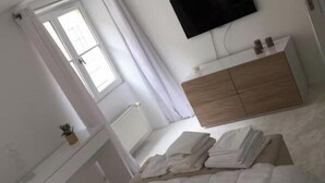 A bedroom with a bed, a bedside table with a plant, a dresser, a TV mounted on the wall, and a window with curtains. - AN EXCEPTIONAL PARISIAN EXPERIENCE CLOSE TO ODEAN & LUXEMBOURG – SAINT GERMAIN (Paris)