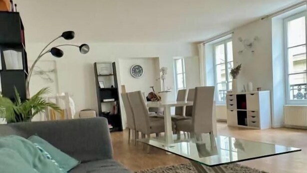 A modern living room with a grey sofa, a glass coffee table, and a dining area with a white table and chairs. - AN EXCEPTIONAL PARISIAN EXPERIENCE CLOSE TO ODEAN & LUXEMBOURG – SAINT GERMAIN (Paris)