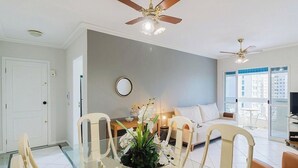 A modern living room with a dining area, a ceiling fan, a large window, and a view of the city. - 3-bedroom Apt Only 300m From the Beach Ejs0803 (Balneário Camboriú)