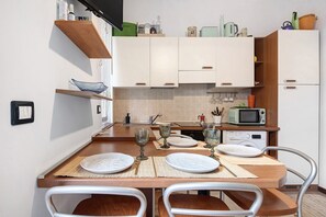 Une cuisine compacte avec des meubles blancs, un four à micro-ondes et une table à manger dressée avec des assiettes et des verres.