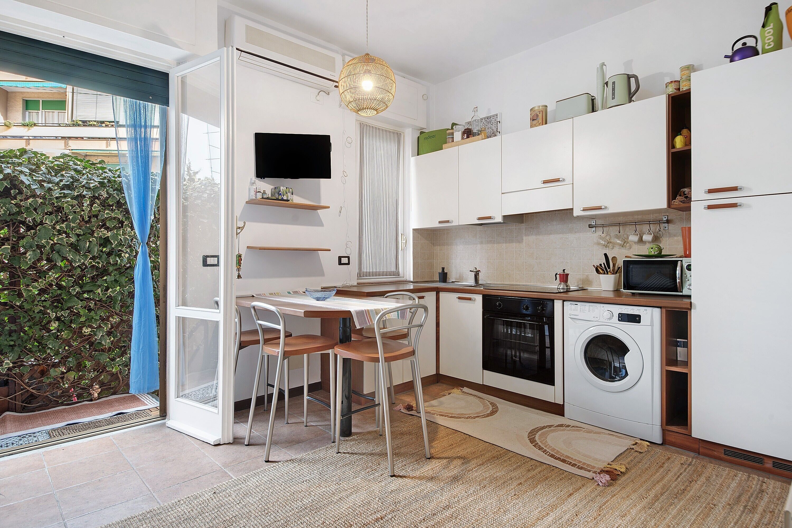 A compact kitchen with a washing machine, microwave, and a dining area with chairs.