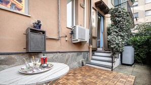 Une terrasse avec une table, un pot de fleurs et un climatiseur fixé au mur.