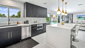 A modern kitchen with dark cabinets, a white countertop, and a large island. There are pendant lights, a built-in oven, and a sink. - Luxury 3 bed 2 bath pool spa home with 29 day minimum (Palm Desert)