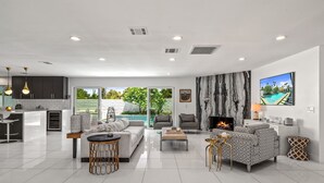 A modern living room with a fireplace, a dining area, and a kitchen with a large island. - Luxury 3 bed 2 bath pool spa home with 29 day minimum (Palm Desert)