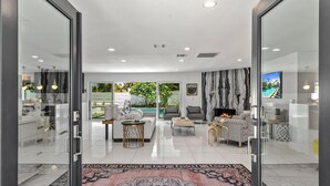 A modern living room with a fireplace, a large window, and a view of a pool. - Luxury 3 bed 2 bath pool spa home with 29 day minimum (Palm Desert)