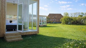A modern, wooden cabin with large glass doors leading to a bedroom with a bed and a small table.