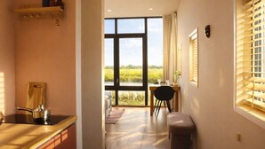 A kitchen with a large window, a dining area with a table and chairs, and a view of a field. - Tiny House Geau near Leeuwarden - for 2, private terrace (Weidum)