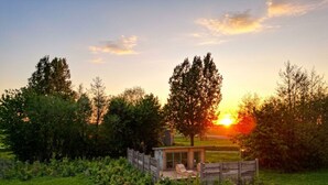 Eine rustikale Holzhütte mit überdachter Veranda und einem einzelnen Stuhl, umgeben von einem Holzzaun und üppigem Grün.