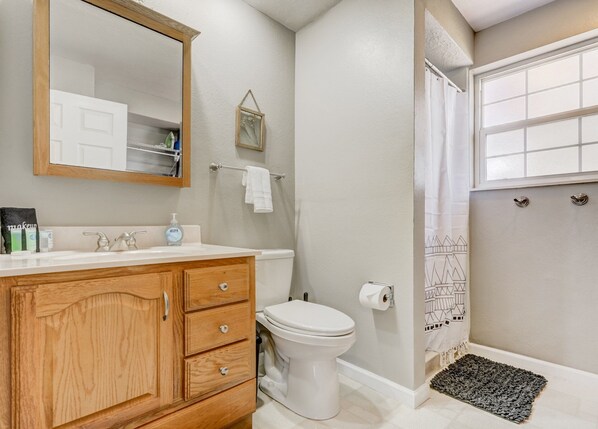 A bathroom with a wooden vanity, a white toilet, a mirror, and a shower curtain with a geometric pattern. - 2242 Ptarmigan (Colorado Springs)