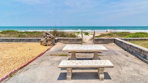 Une vaste plage de sable fin, avec une vue dégagée sur l’océan, une table de pique-nique et un muret en pierre.