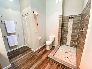A bathroom with a toilet, a shower with a stone tile wall, and wooden flooring. - 2622 N Nevada (Colorado Springs)