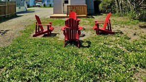 Une petite maison avec un porche à l’avant et deux fauteuils Adirondack rouges.