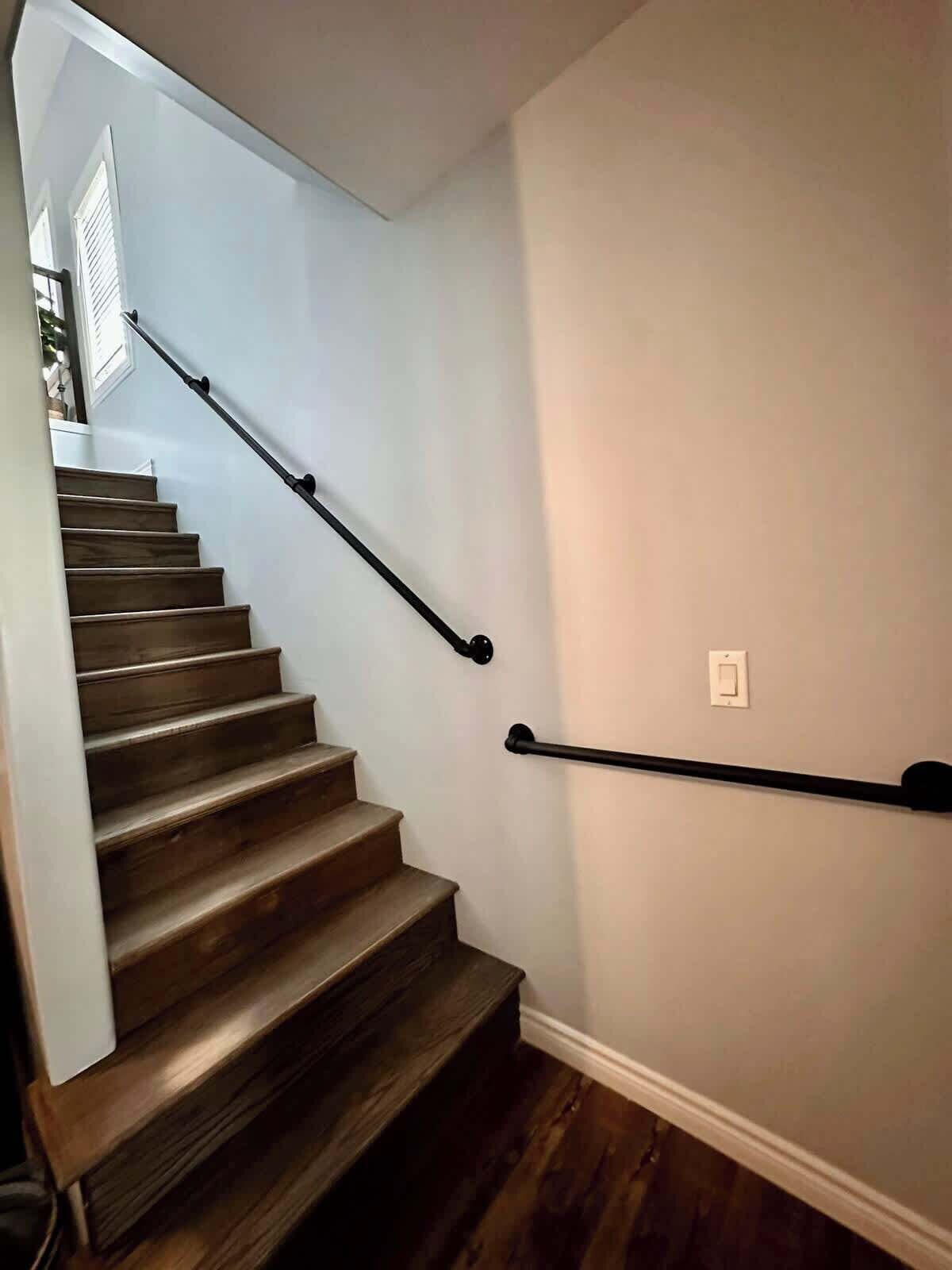 A wooden staircase with a handrail, white walls, and a white electrical outlet.