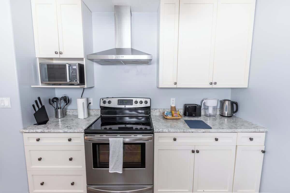 Una cocina con gabinetes blancos, estufa de acero inoxidable, microondas y cafetera.