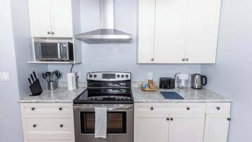 Una cocina con gabinetes blancos, estufa de acero inoxidable, microondas y cafetera.