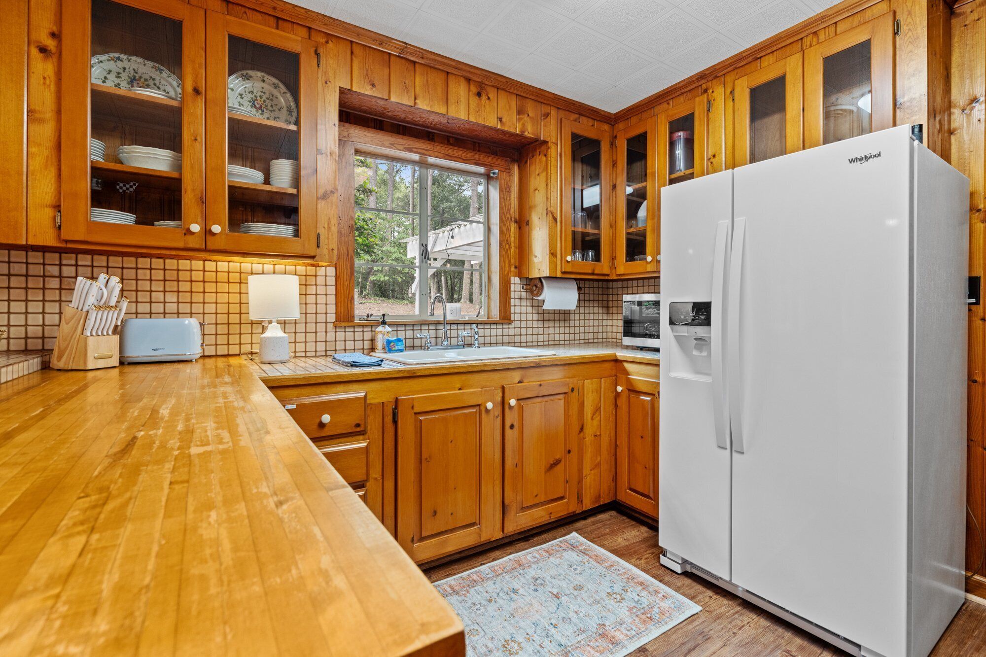 A kitchen with wooden cabinets, a white refrigerator, a window, and a tiled backsplash.