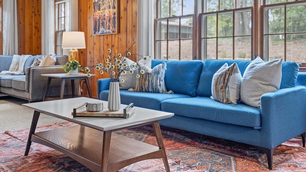 Ein Wohnzimmer mit einem blauen Sofa, einem Couchtisch, einer Lampe und einem Gemälde an der Wand.