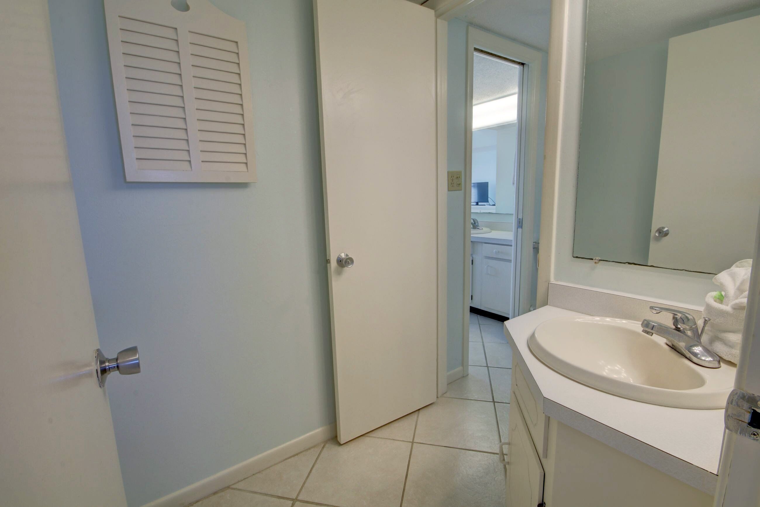 Ein Badezimmer mit einem weißen Waschbecken, einem Spiegel und einer Tür mit einem durchbrochenen Fenster.