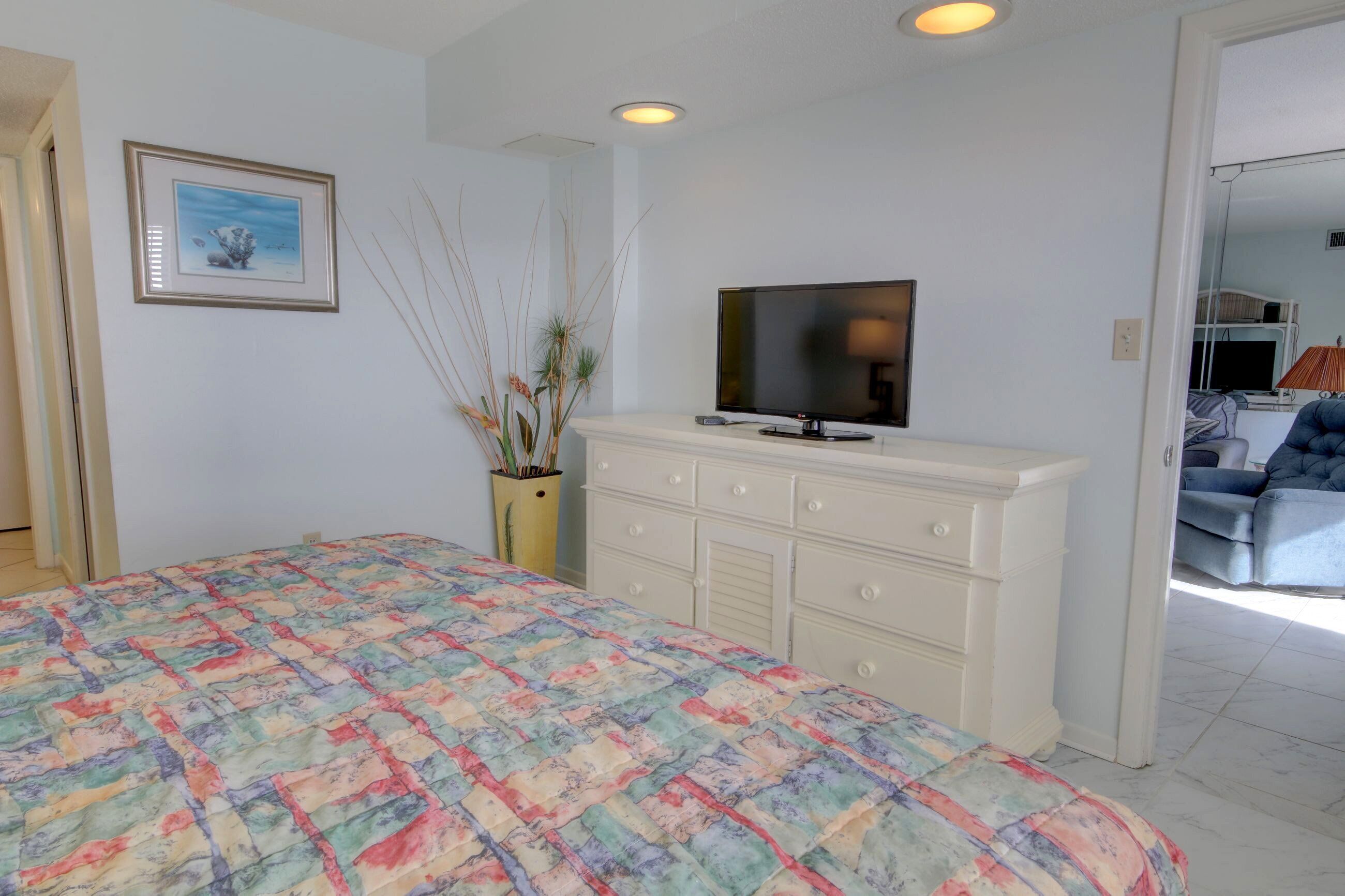 A bedroom with a bed, a dresser, a television, and a framed picture on the wall.
