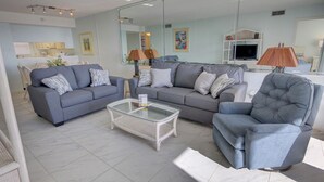 Ein modernes Wohnzimmer mit einem grauen Sofa, einem Glastisch und einem grauen Sessel.