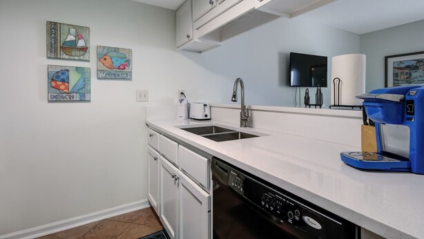Una cocina moderna con armarios blancos, lavavajillas, cafetera y un televisor de pantalla plana montado en la pared.