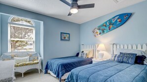 Un dormitorio con dos camas, ventilador de techo, ventana con persianas y una decoración con una tabla de surf.