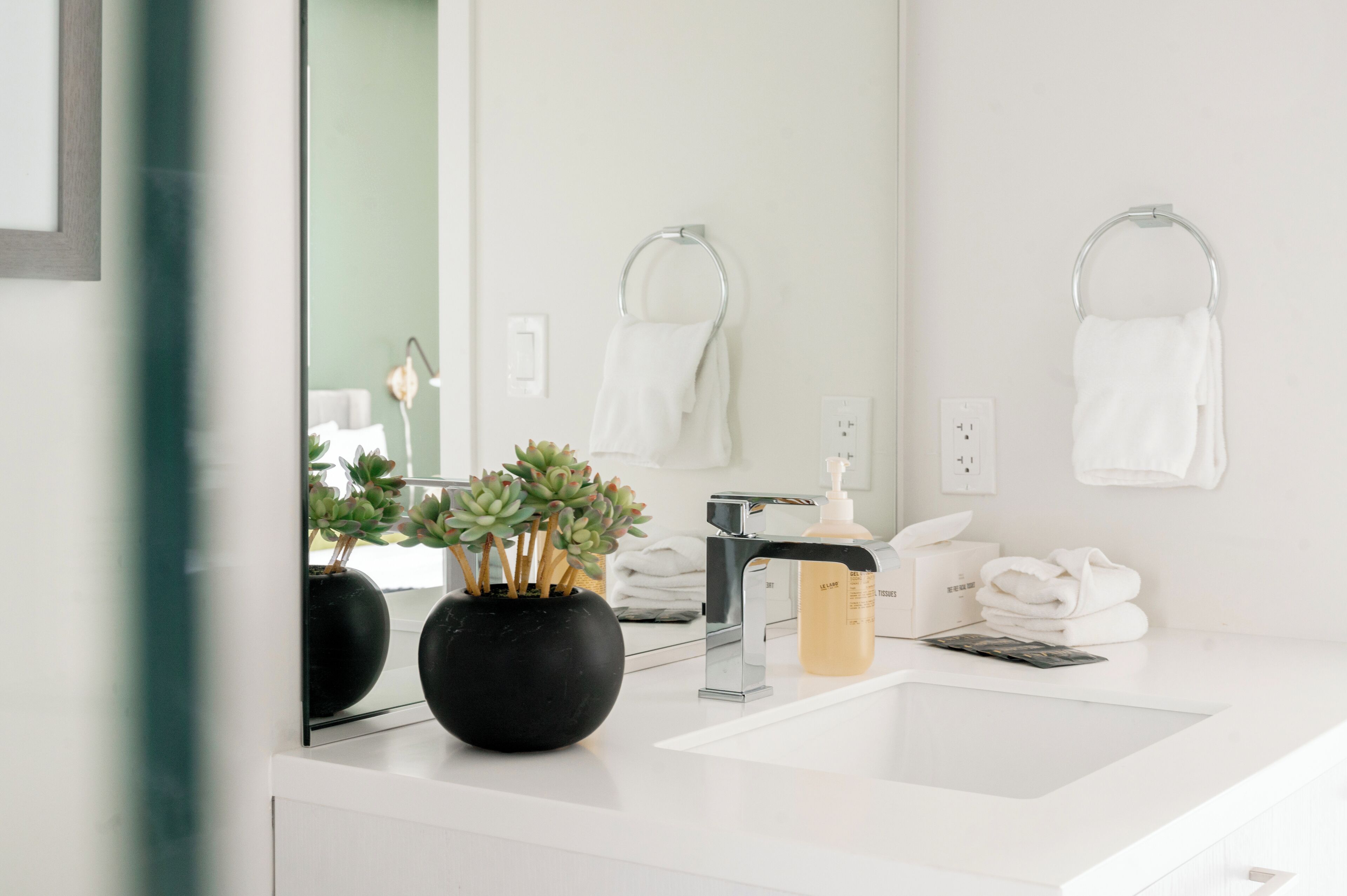 Een moderne badkamer met een witte wastafel, een spiegel en twee zwarte vazen met vetplanten.