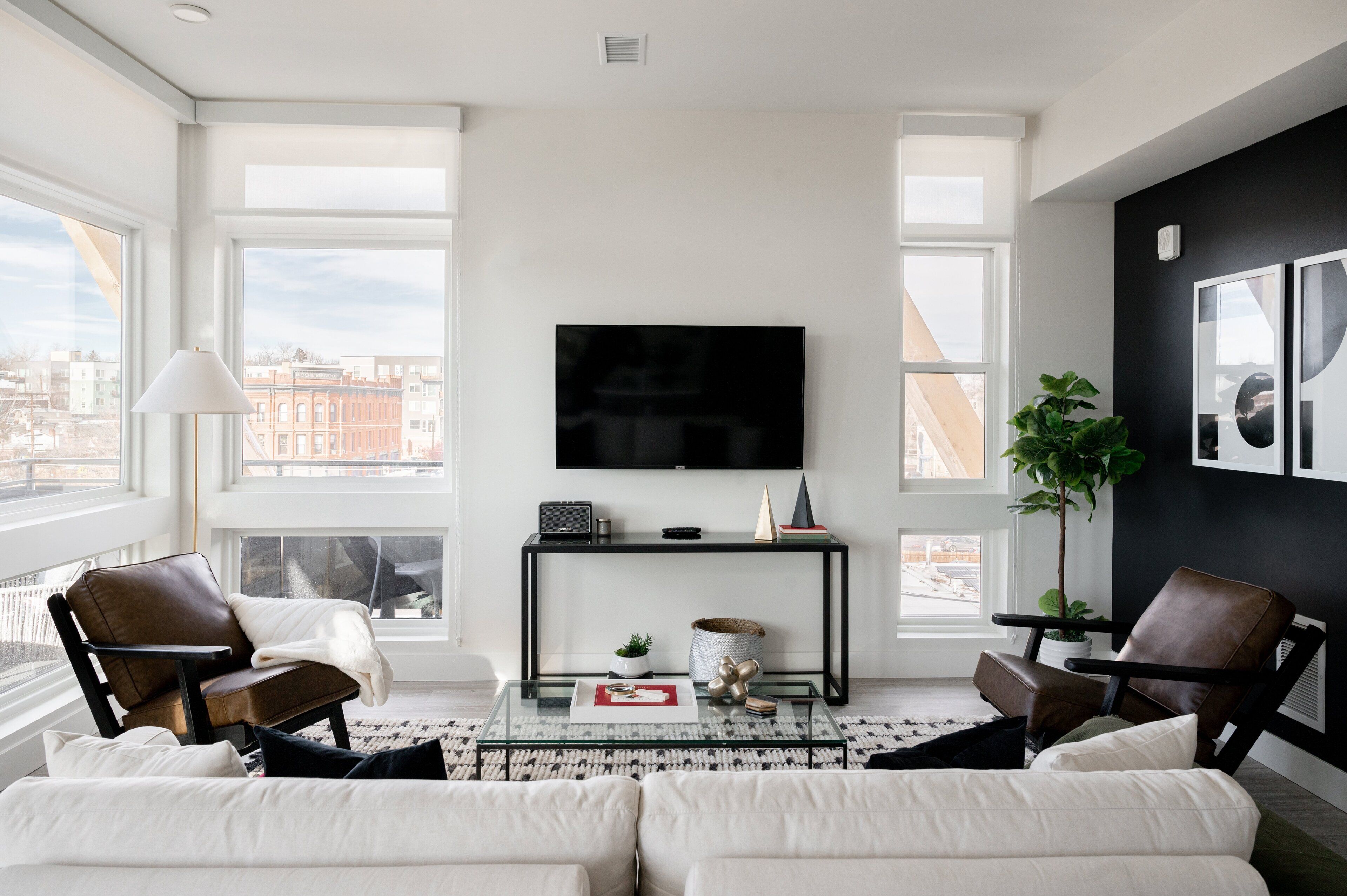 Ein modernes Wohnzimmer mit großem Fenster, Flachbildfernseher, Glastisch und Ledersesseln.