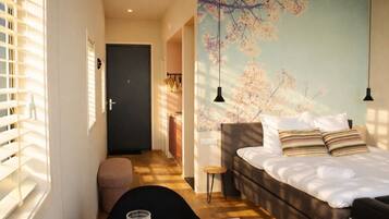 Habitación de hotel con una cama, un escritorio con una silla, un taburete pequeño y un mural de flores de cerezo en la pared.