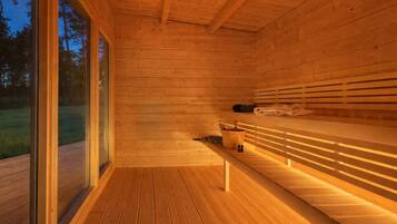 Een houten sauna met banken en een houten vloer, grote ramen en uitzicht op de omgeving.