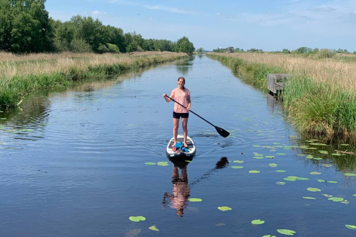Una persona haciendo paddleboard en un canal estrecho rodeado de abundante vegetación.