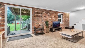 A living room with a brick wall, a sliding glass door leading to a backyard, a flat-screen TV, and a coffee table. - 2 min to AUD | Private Getaway w/ Firepit (Kitchener)