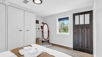 Une chambre à coucher avec un lit, une armoire, un miroir, une porte et une fenêtre.