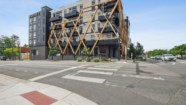 Ein modernes Gebäude mit einer markanten, geometrischen Fassade, einer Fußgängerampel und blauem Himmel.