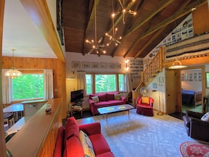 Un accogliente soggiorno con soffitto in legno, un divano rosso, una televisione e un'area pranzo con tavolo in legno.