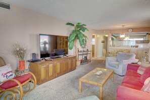A living room with a television, wooden cabinet, wicker chair, and a large plant. - 240 El Matador (Fort Walton Beach)