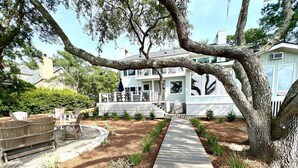 Une terrasse en bois menant à une maison dotée d’un porche abrité et d’un espace salon extérieur.