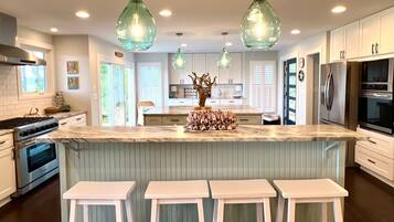 A modern kitchen with white cabinets, a marble island with bar stools, pendant lighting, and stainless steel appliances.