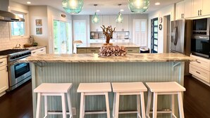 Une cuisine moderne avec des armoires blanches, un comptoir en marbre et des luminaires suspendus.