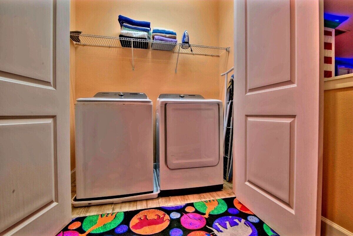 A laundry room with two washing machines, a drying rack with folded clothes, and a colorful rug on the floor.
