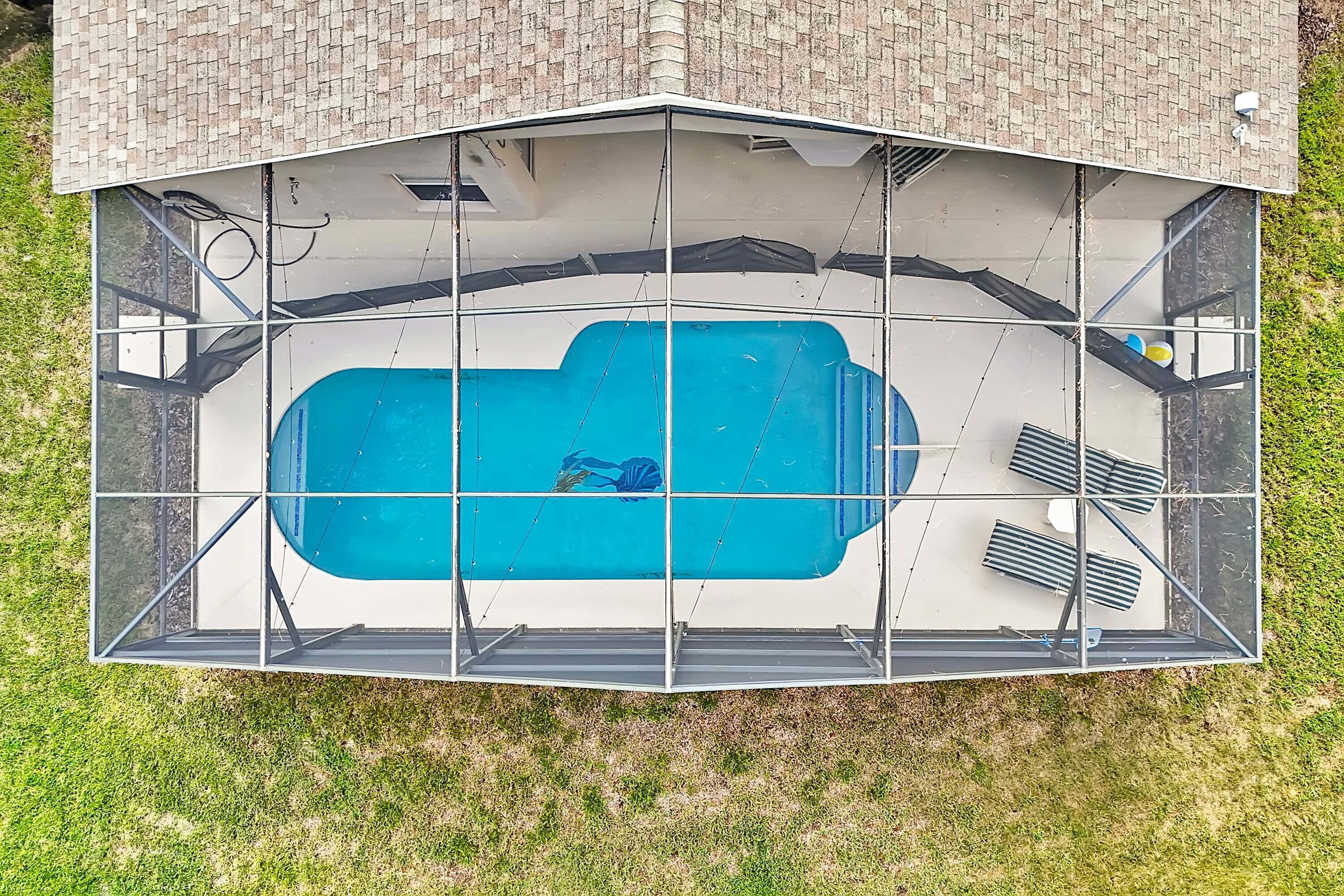 Une piscine entourée d’une clôture de sécurité en métal, bordée d’une pelouse et d’un bâtiment en briques.