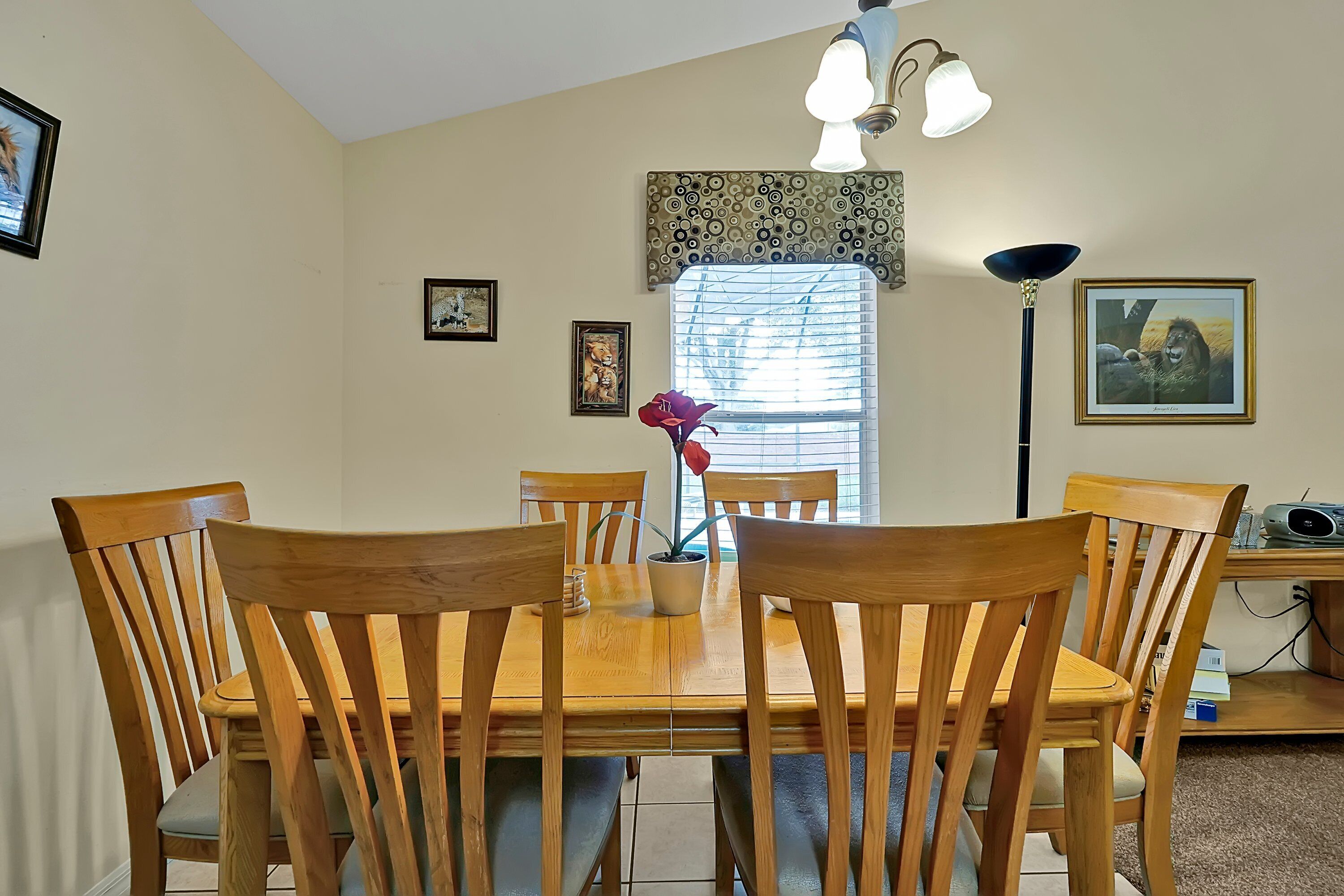 A dining area with a wooden table and chairs, a potted plant, and a window with blinds.