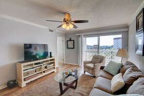 A living room with a television, a ceiling fan, a sofa, a chair, and a window with a view of buildings. - 243 El Matador (Fort Walton Beach)