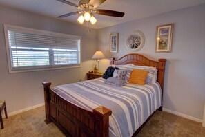A bedroom with a wooden bed, a ceiling fan, a window with blinds, and two wall-mounted lamps. - 243 El Matador (Fort Walton Beach)